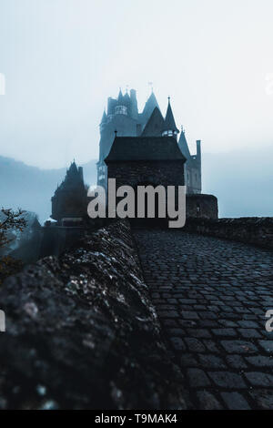 Ingresso anteriore di Burg Eltz / Castello Eltz con storico ingresso di gate durante ore blu durante una nebbiosa giornata autunnale con coperto nebbia Castello (Germania) Foto Stock