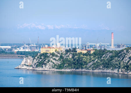 Castello di Duino e il porto di Monfalcone con le montagne delle Alpi in background in Italia, Europa Foto Stock