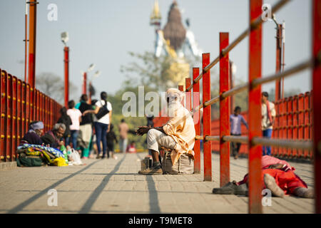 Un povero Sadhu è chiedere denaro in Haridwar, India. Sfumata del signore Shiva in background. Foto Stock