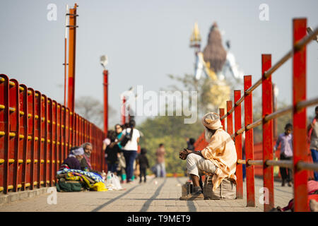 Un povero Sadhu è chiedere denaro in Haridwar, India. Sfumata del signore Shiva in background. Foto Stock