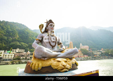 Splendida vista della statua di seduta signore Shiva sulla sponda del fiume Gange. Sfocato Trimbakeshwar tempio in background. Foto Stock