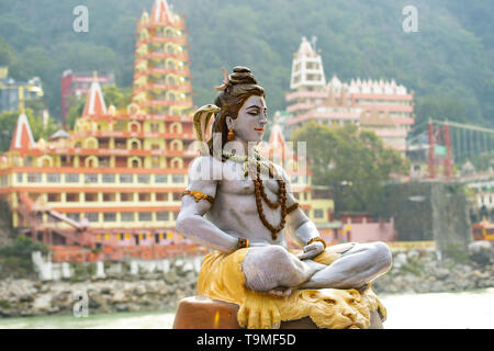 Splendida vista della statua di seduta signore Shiva sulla sponda del fiume Gange. Sfocato Trimbakeshwar tempio in background. Foto Stock