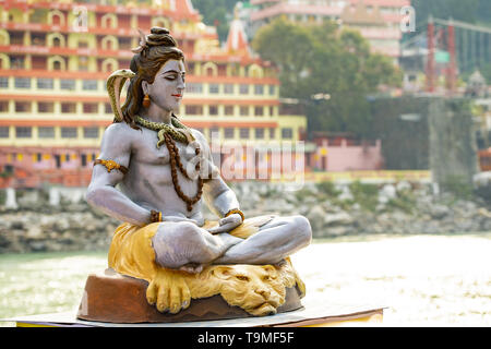 Splendida vista della statua di seduta signore Shiva sulla sponda del fiume Gange. Sfocato Trimbakeshwar tempio in background. Foto Stock