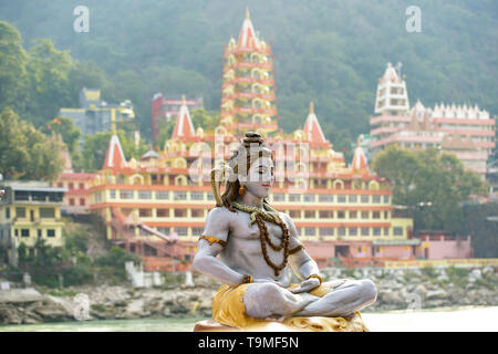 Splendida vista della statua di seduta signore Shiva sulla sponda del fiume Gange. Sfocato Trimbakeshwar tempio in background. Foto Stock