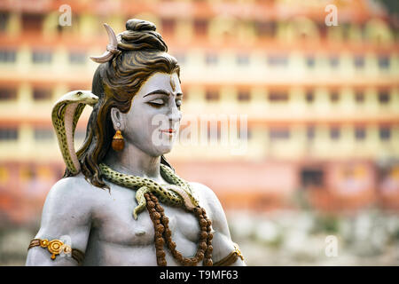 Splendida vista della statua di seduta signore Shiva sulla sponda del fiume Gange. Sfocato Trimbakeshwar tempio in background. Foto Stock