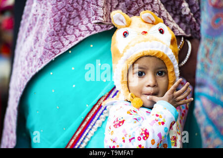 Ritratto di una bella timido bambino con un cappello spiritoso tenendo la madre mano a Varanasi. Foto Stock