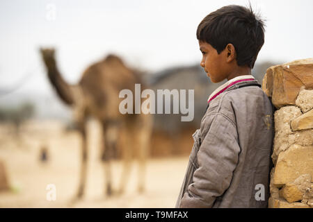 Un bambino è appoggiata contro un muro mentre un cammello è in background. Foto Stock