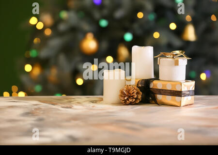 Regali di Natale con candele accese sulla tavola a colori contro le luci sfocate Foto Stock