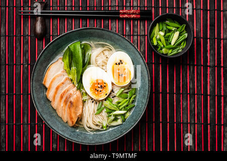 Ramen zuppa di noodle al pollo con uovo e sul tappetino di bambù. Tabella vista dall'alto. Cucina asiatica food Foto Stock