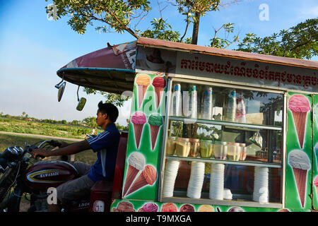 Un giovane uomo cambogiano o adolescente comanda una motocicletta tirando un gelato il rimorchio su una autostrada al di fuori di Siem Reap, Cambogia. Foto Stock