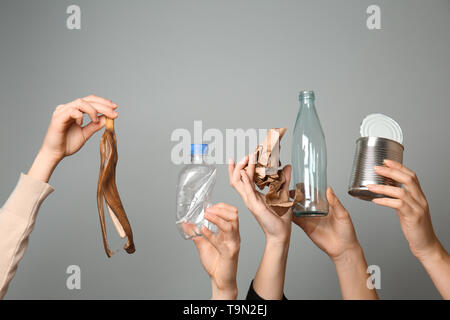 Molte mani con i diversi tipi di rifiuti su sfondo grigio. Concetto di ecologia Foto Stock