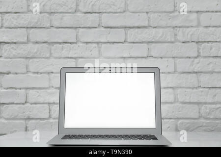 Laptop moderno sulla tavola bianco contro un muro di mattoni Foto Stock