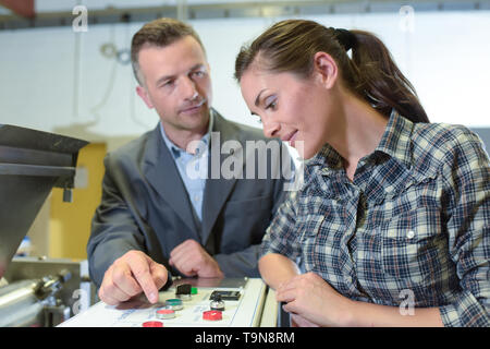 Supervisore di fabbrica che mostra femmina partecipante i comandi delle macchine Foto Stock