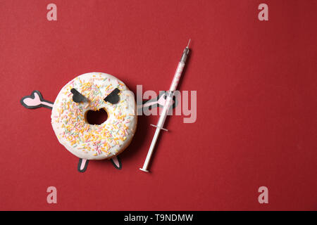 Arrabbiato ciambella con siringa sul colore di sfondo. Concetto di dipendenza Foto Stock