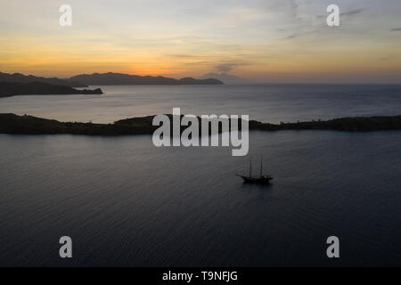 Un tradizionale Pinisi schooner vele al tramonto nel Parco Nazionale di Komodo, Indonesia. Questa area tropicale è noto per la sua biodiversità marina. Foto Stock