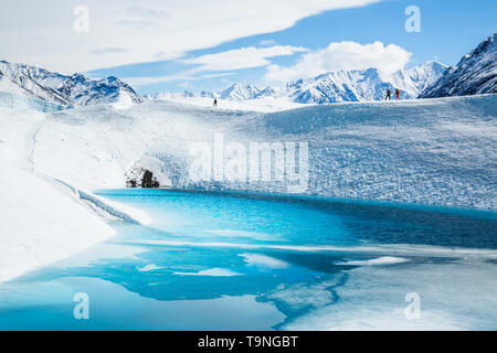 Te scalatori trekking attraverso il ghiacciaio Matanuska oltre un profondo lago blu sulla parte superiore del ghiacciaio in Chugach Mountains. Foto Stock