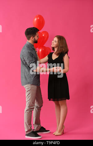 Amare giovane coppia con palloncini in forma di cuore su uno sfondo colorato. Celebrazione del giorno di San Valentino Foto Stock