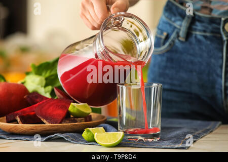 Donna versando gustoso succo dalla brocca in vetro su di un tavolo luminoso Foto Stock