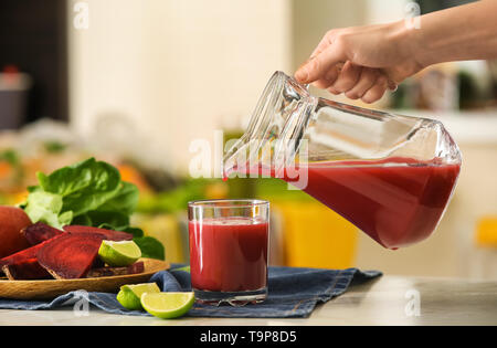 Donna versando gustoso succo dalla brocca in vetro su di un tavolo luminoso Foto Stock