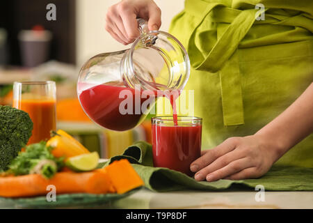 Donna versando gustoso succo dalla brocca in vetro sul tavolo Foto Stock