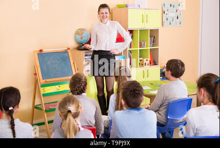 Giovani insegnanti di sesso femminile in piedi alla lavagna di una classe, conducendo la lezione con i bambini Foto Stock
