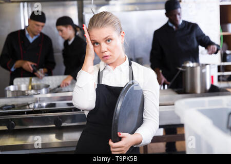 Infelice e stanco giovane cameriera in attesa ordinato piatti nel ristorante cucina Foto Stock