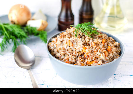 Farinata di grano saraceno con carote e prezzemolo nella piastra di blu. Sullo sfondo delle cipolle dorate,verde il prezzemolo e il sale e il pepe mills. Foto Stock