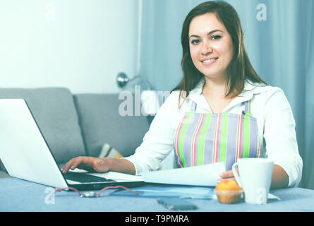 Giovane donna navigando attraverso utili suggerimenti per la cottura in Internet Foto Stock