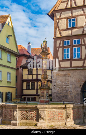 Bella vista della fontana di San Giorgio, costruita nel 1446 presso la piazza del mercato di fronte a semi-case con travi di legno a Rothenburg ob der Tauber, Germania. La... Foto Stock