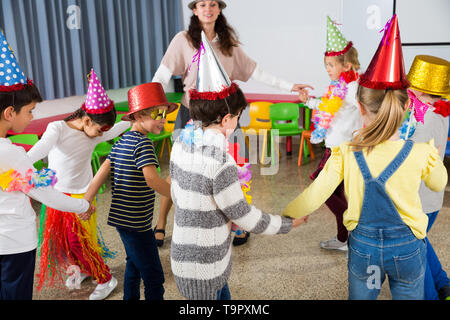 Felice di ridere gli alunni della scuola primaria per divertirsi durante il festoso evento con il loro insegnante femminile, balli di gruppo Foto Stock