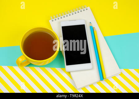 Vista dall'alto per notebook vuoto con foglio di carta bianco, smartphone,matite e la tazza di tè Foto Stock