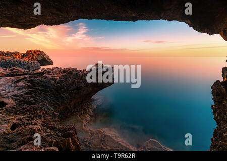 Un tramonto meraviglioso immagine di Cape Greco scogliere e rocce su un tramonto nella città di Paralimni, Cipro. Colorato di rosso, rosa e giallo skies con mare blu turchese. Foto Stock