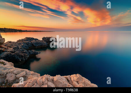 Un tramonto meraviglioso immagine di Cape Greco scogliere e rocce su un tramonto nella città di Paralimni, Cipro. Colorato di rosso, rosa e giallo skies con mare blu turchese. Foto Stock