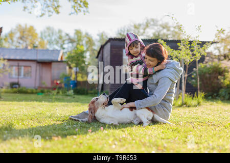 Nonna con nipote e cane giocando sul prato per prendere il sole. Soleggiata giornata di primavera nel villaggio. Foto Stock