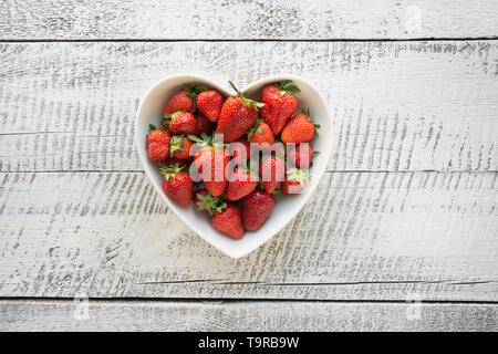 Mature fragola organico nella piastra come cuore isolato su bianco sullo sfondo di legno. Vista da sopra. Foto Stock