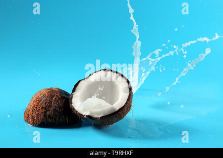 Metà di cocco fresco e splash di latte sul colore di sfondo Foto Stock