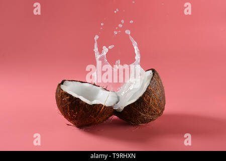 Metà di cocco fresco e splash di latte sul colore di sfondo Foto Stock