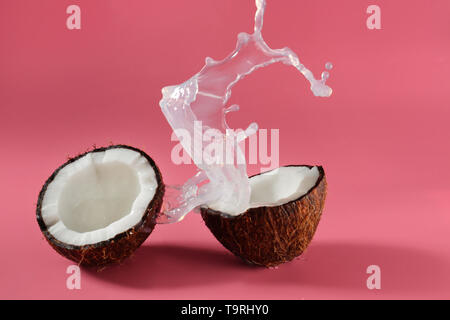 Metà di cocco fresco e splash di latte sul colore di sfondo Foto Stock