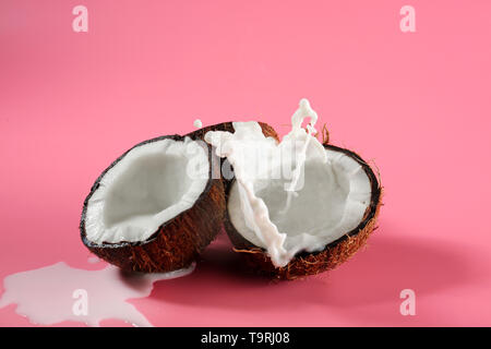 Metà di cocco fresco e splash di latte sul colore di sfondo Foto Stock