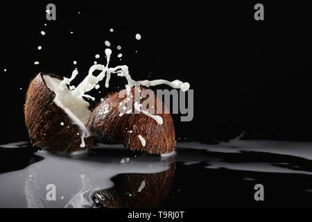 Metà di cocco fresco e splash di latte su sfondo scuro Foto Stock