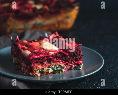 Ortaggio pranzo Rainbow lasagne su sfondo scuro.idee e ricette per vegetariani sani la cena o il pranzo.Le Lasagne con le barbabietole, zucca, funghi, ricotta e spinaci, mozzarella. Copia spazio per il testo Foto Stock