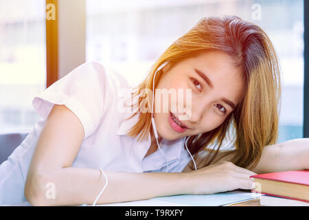 Carino young teen università asiatiche ragazza in uniforme la lettura di libro in biblioteca Foto Stock