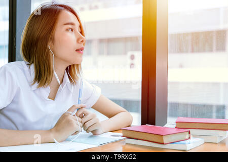 Carino young teen università asiatiche ragazza in uniforme la lettura di libro in biblioteca Foto Stock