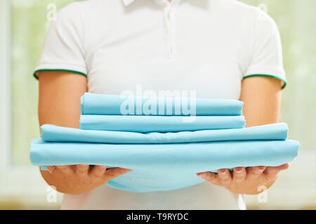 Una donna può contenere una pila di pulire ripiegato biancheria blu. Sfondo sfocato. Close-up. Foto Stock