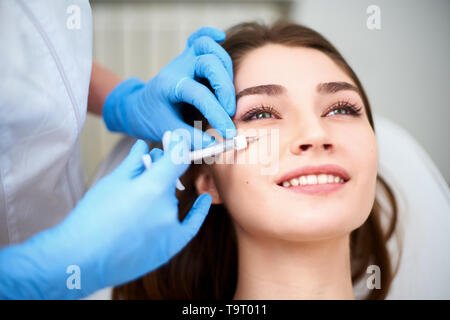 Dottore in guanti medicali con siringa inietta botulinum sotto gli occhi per il ringiovanimento di trattamento delle rughe. Iniezione di riempimento per occhio rughe la levigatura Foto Stock