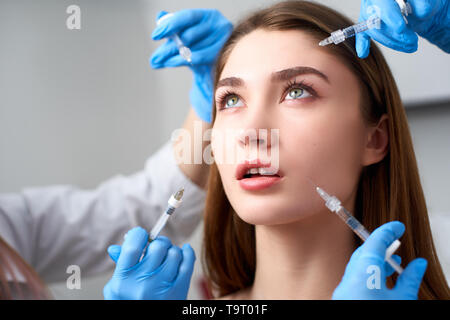 Mani di estetiste siringhe di contenimento intorno la bambola come donna faccia per iniezione in cosmetologia clinica. Modello femminile con occhi vuoti sotto influenza di Foto Stock