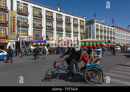 Un pedicab porta un passeggero di fronte appartamenti moderni con disegni tradizionali a Lhasa, in Tibet. Foto Stock