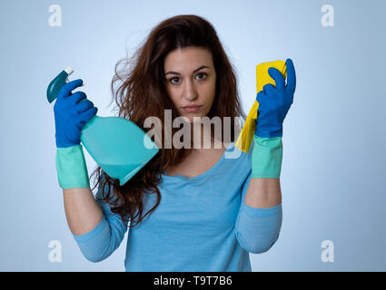 Giovani belle sconvolto casalinga donna tenendo la benna mop spray per la pulizia di sensazione ha sottolineato stanco e deluso in compiti domestici e i ruoli di genere conc Foto Stock