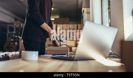 Ritagliato shot dell uomo la scansione del codice a barre di spedizione al suo banco. Uomo che lavora in una goccia di spedizione ufficio, la preparazione di un pacco a consegnare al cust Foto Stock