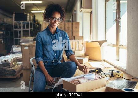 Sorridente giovane donna di imballare il prodotto in una scatola per la spedizione al cliente. Business online proprietario lavorando in ufficio. Foto Stock